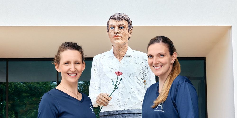 Das Psychiatrie-Podcast-Team Cindy und Sabine vor dem Mann mit Rose am Alexius/Josef Krankenhaus